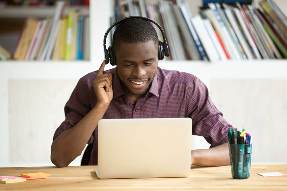 smiling man watching a laptop video through headphones