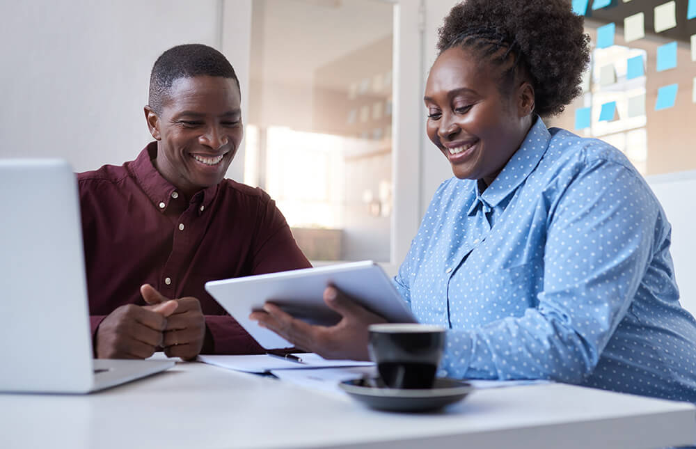 smiling couple at table with tablet and laptop